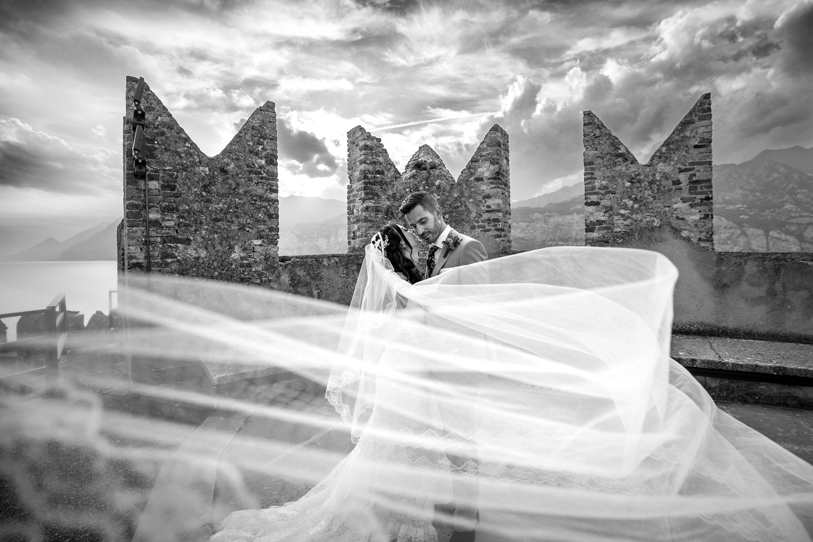 Bride and groom embracing during a wedding at Castello di Malcesine, with the veil flowing in the wind overlooking Lake Garda