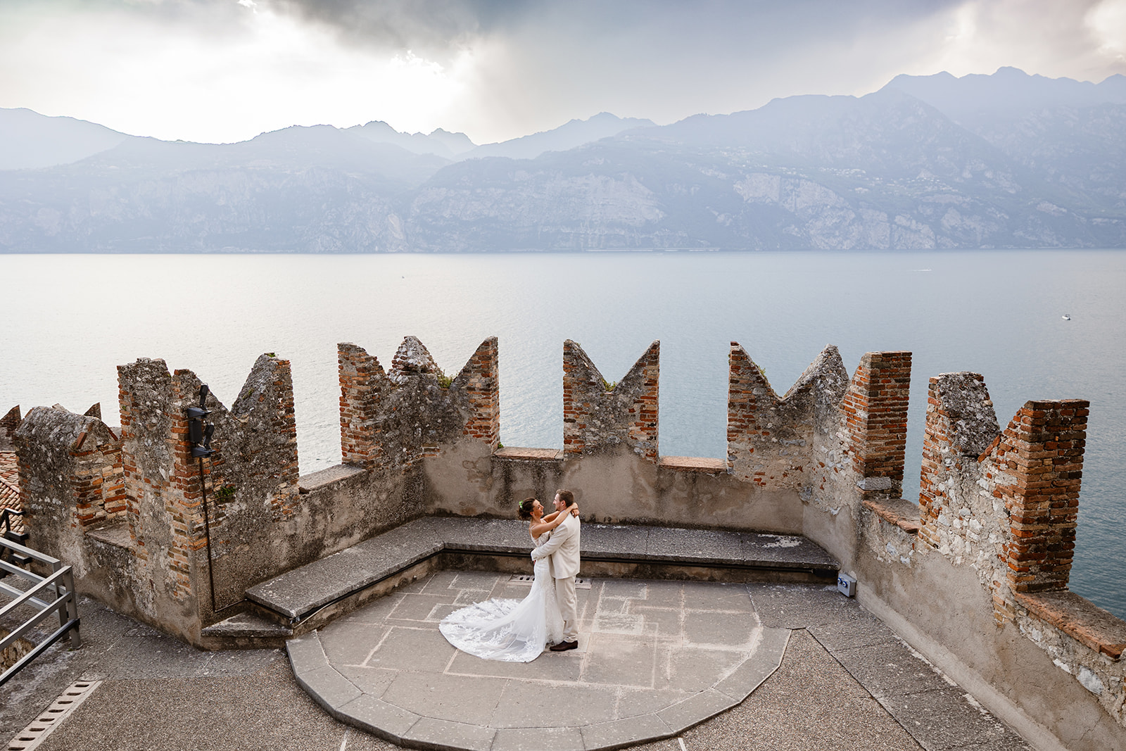 Bride and groom embracing on the terrace of Castello di Malcesine with Lake Garda and the Alps in the background, destination Lake Garda Wedding Photographer